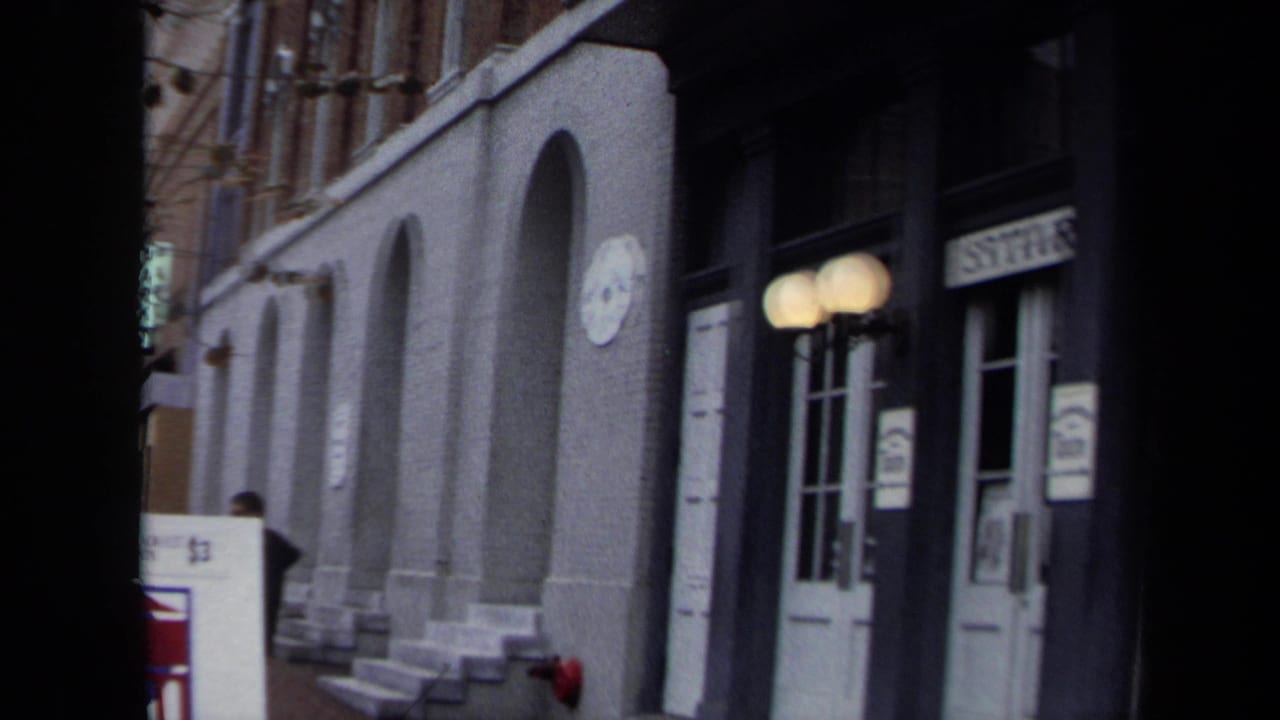 Street-level view of arched building entrances with white doors and globe lamps.