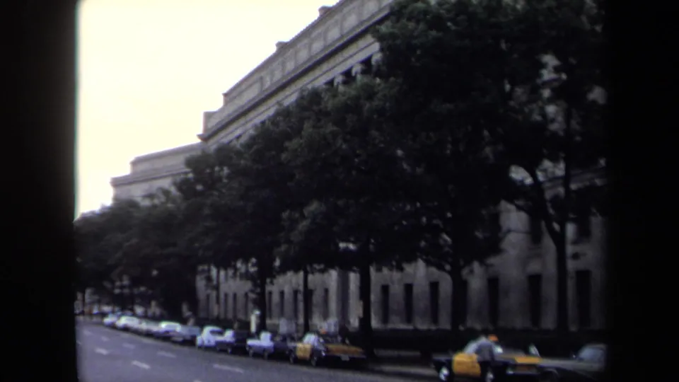 1970 Washington, DC street view with trees, parked cars, a yellow taxi, and a large building facade along the block.
