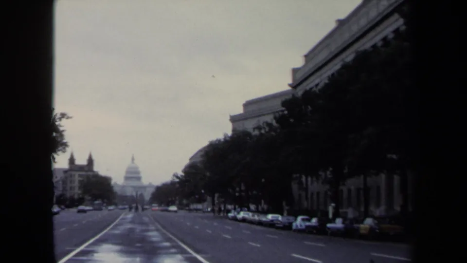 Washington, DC avenue view with the U.S. Capitol centered in the distance and parked cars lining both sides.