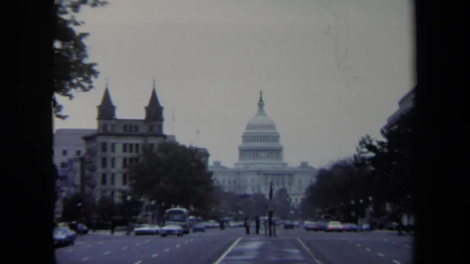 1970 Washington, DC street view looking toward the U.S. Capitol, with period cars, pedestrians, trees, and buildings in frame.