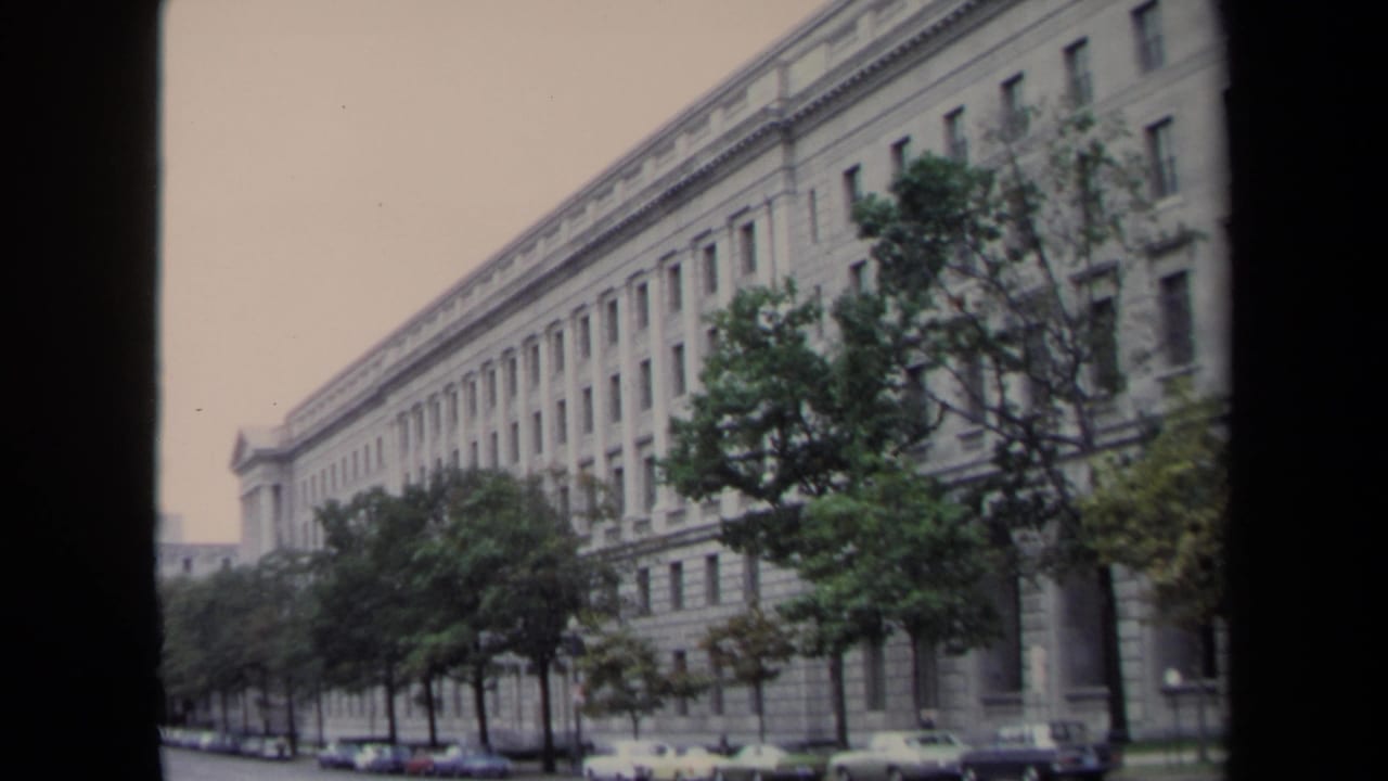 Tree-lined street view of a large stone building with rows of windows and parked cars.