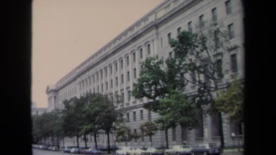 Washington, DC street-level view of a large stone institutional building, trees, and curbside cars in 1970 footage.