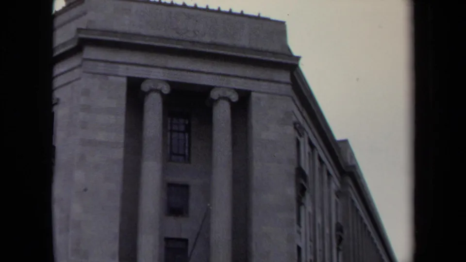 Street-level 1970 Washington, DC frame showing a columned stone building corner with tall windows and a heavy cornice.