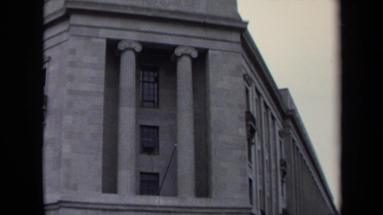 Upper facade of a monumental stone building with tall columns and side windows.