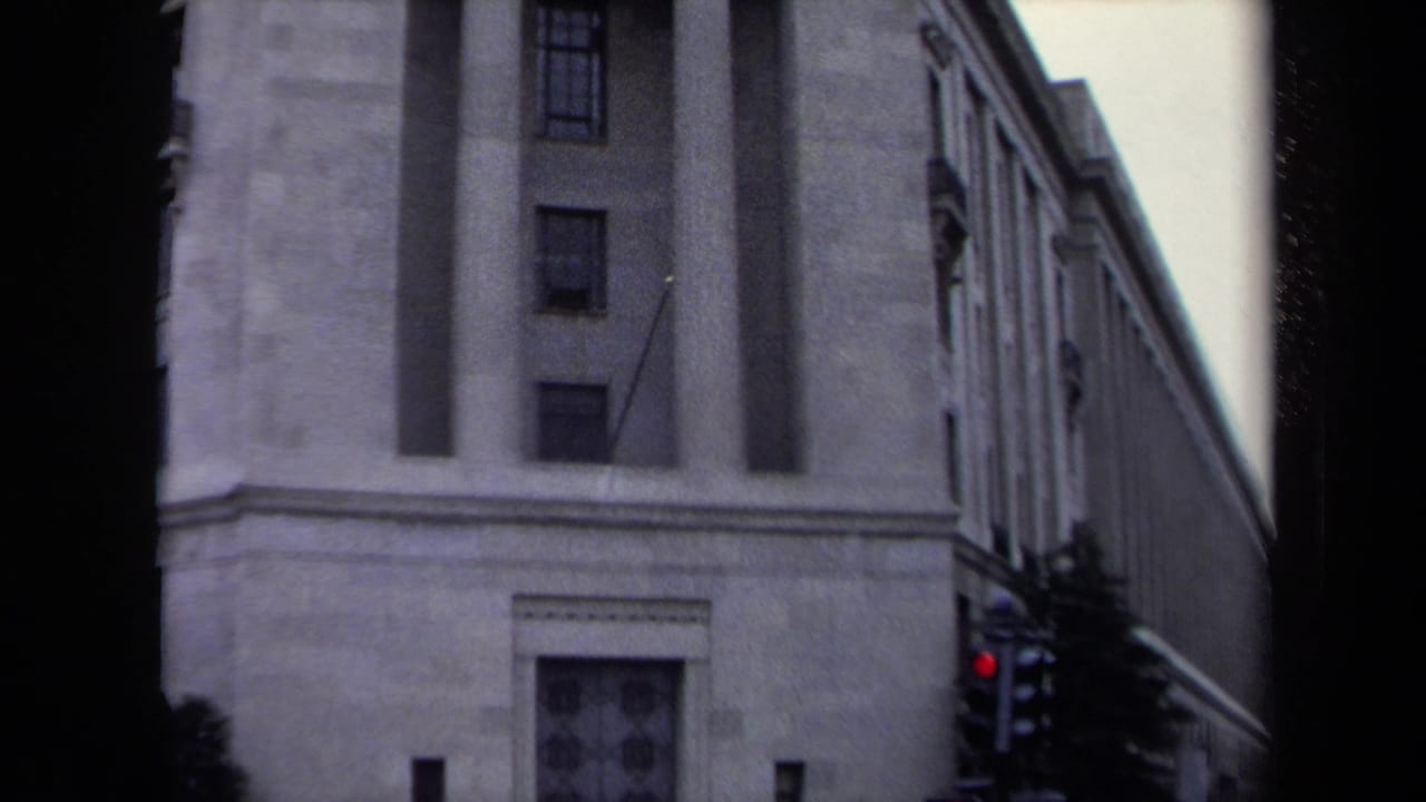 1970 Washington, DC home-movie frame of a monumental stone building facade, with a traffic light and tree visible near street level.