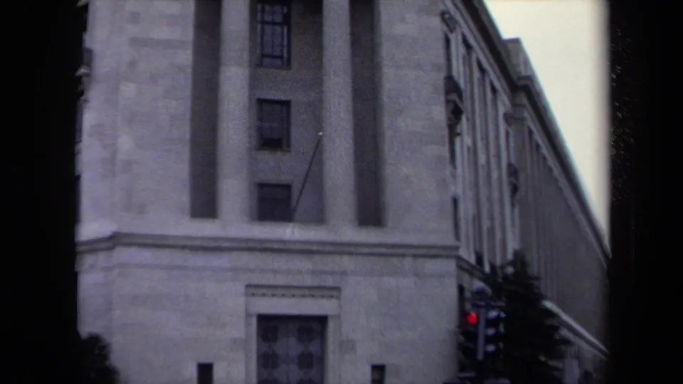 1970 Washington, DC home-movie frame of a monumental stone building facade, with a traffic light and tree visible near street level.