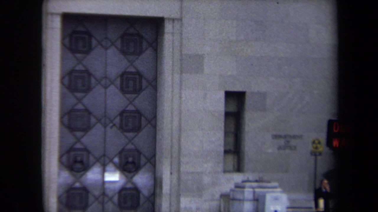 1970 Washington, DC 8mm frame showing a stone facade, decorative double doors, and a glowing pedestrian signal at the edge of the shot.