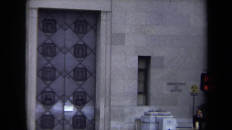1970 Washington, DC 8mm frame showing a stone facade, decorative double doors, and a glowing pedestrian signal at the edge of the shot.