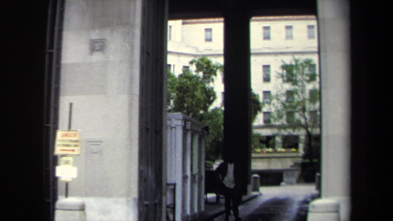 View through a stone archway toward a courtyard with trees and a distant building.