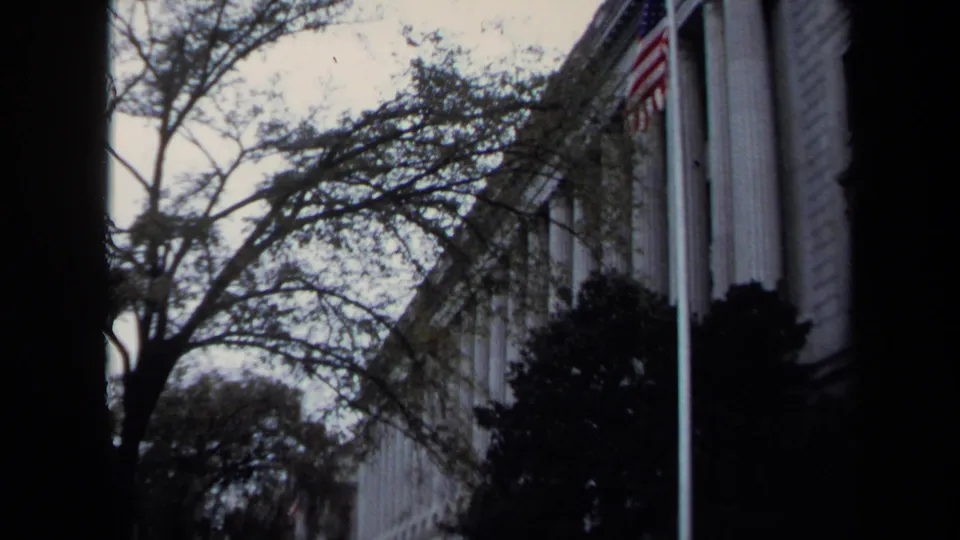 Washington DC exterior view of a formal columned building, trees, shrubs, and a visible American flag on 8mm film.