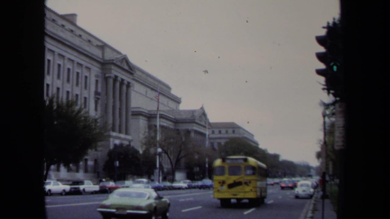 1970 Washington, DC street view with a yellow school bus, classic cars, trees, and a monumental columned public building.