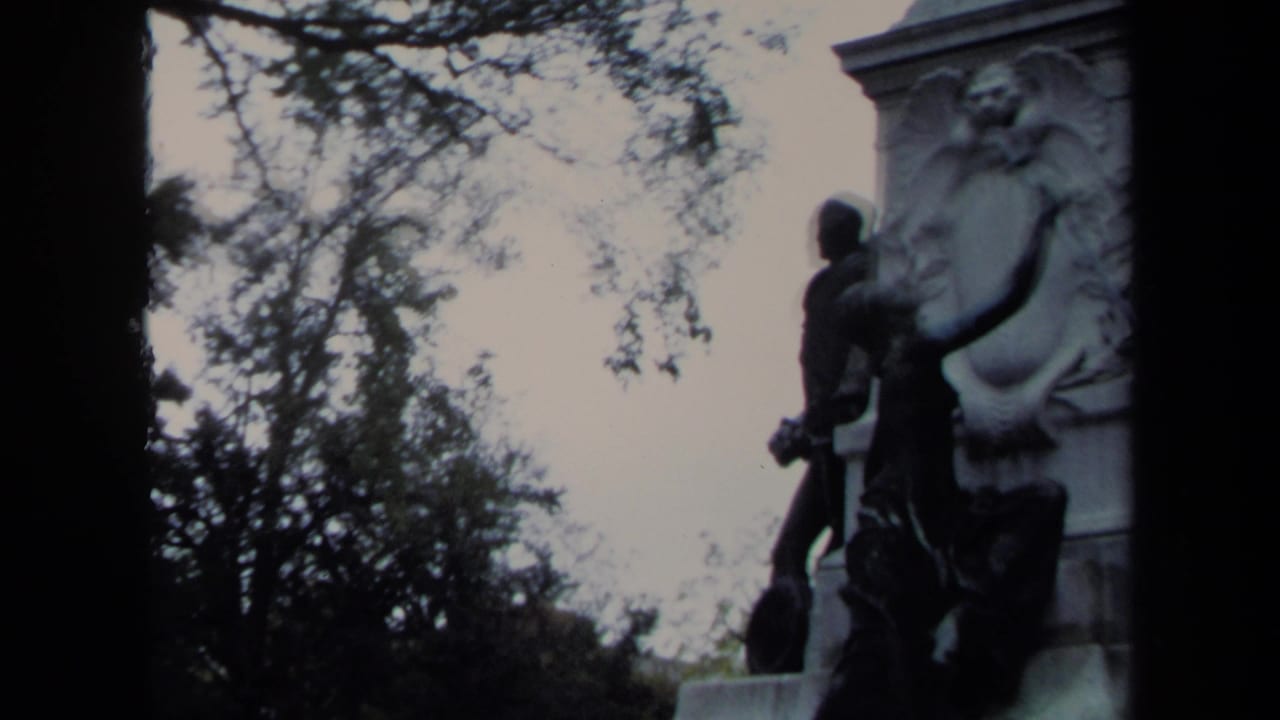 Stone monument with bronze figures and carved reliefs among trees.