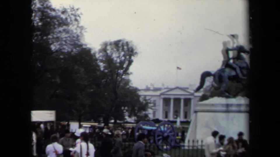 1970 Washington, DC home-movie frame showing visitors near a cannon and equestrian statue with the White House in the background.