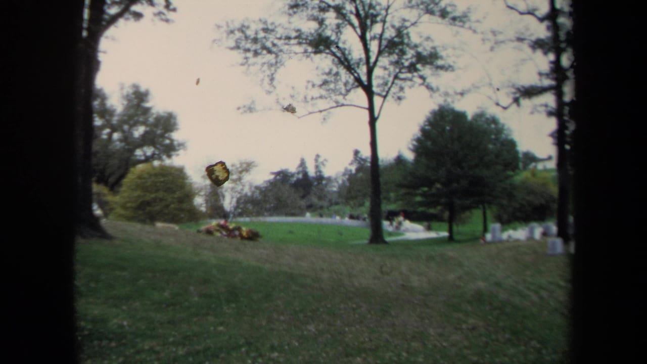 1970 Washington DC park view with grassy hills, mature trees, distant visitors, and a pale curved path seen through dark film-frame edges.