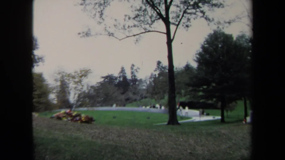1970 Washington DC home-movie frame of a landscaped park, with a broad lawn, trees, a curved walkway, and small distant figures.