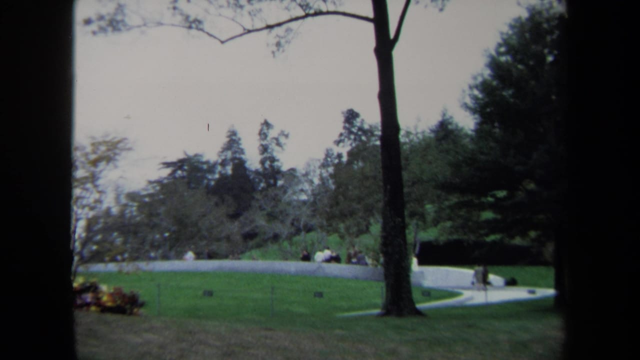 1970 8mm view of a Washington DC park lawn with a curved path, trees, low wall, and small distant visitors.
