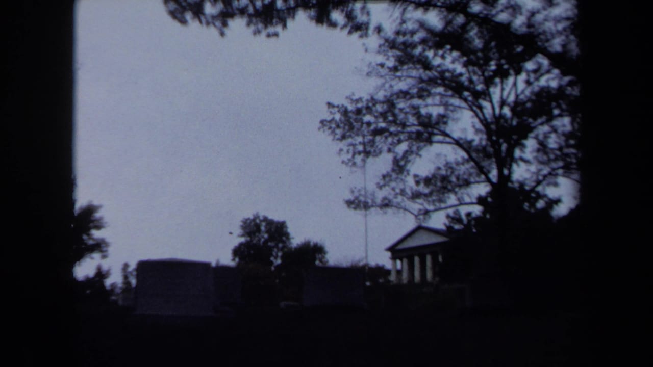 Dim 1970 Washington DC park view with trees silhouetted around a small classical columned building.