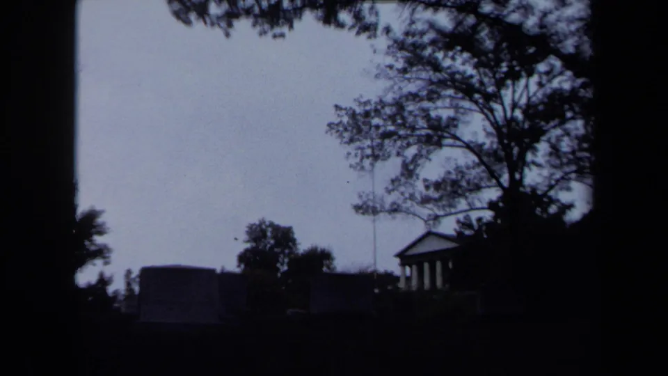 Dim 1970 Washington DC park view with trees silhouetted around a small classical columned building.