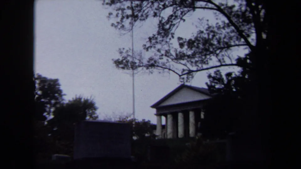 1970 Washington, DC 8mm frame showing a distant columned building, flagpole, lawn, trees, and dark foreground silhouettes.