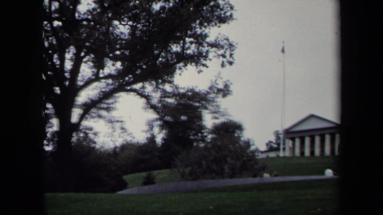 Distant columned building on a grassy hill with a flagpole nearby.