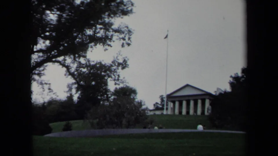 1970 Washington, DC home-movie frame showing a columned landmark beyond a walkway, trees, and grassy foreground.