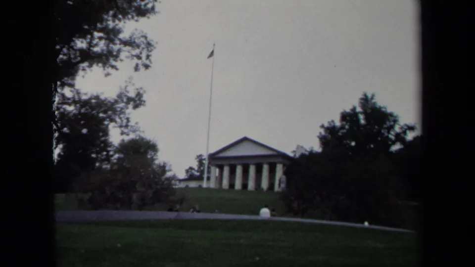Distant 1970 Washington, DC view of a columned building and flagpole, with tiny seated people visible on the grass.