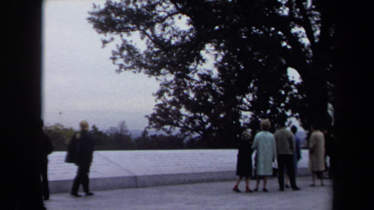 A man walks past a white wall while small groups stand near trees.