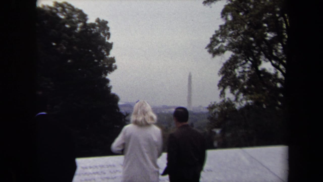 1970 8mm frame of two visitors facing a distant Washington Monument from a memorial overlook in Washington, DC.