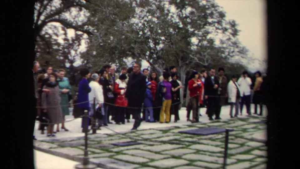 A group of visitors in 1970s clothing stands along a roped walkway at a Washington, DC memorial site.