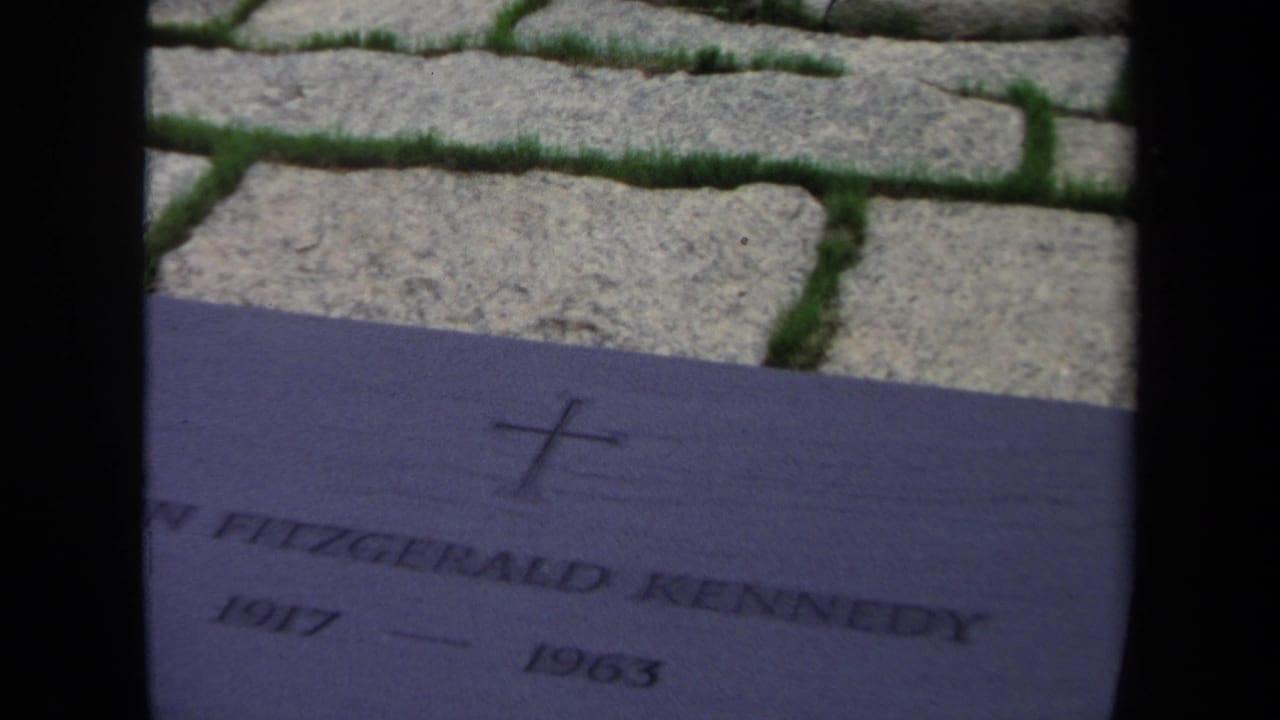 Engraved John Fitzgerald Kennedy plaque beside cobblestones and grass.