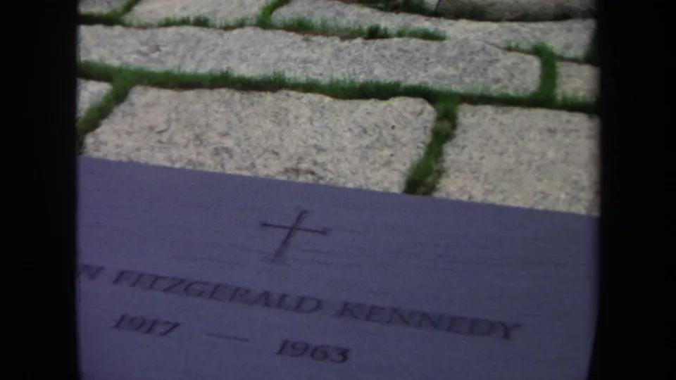 1970 Washington, DC 8mm frame showing the John Fitzgerald Kennedy grave plaque, cross mark, cobblestone paving, and grass seams.