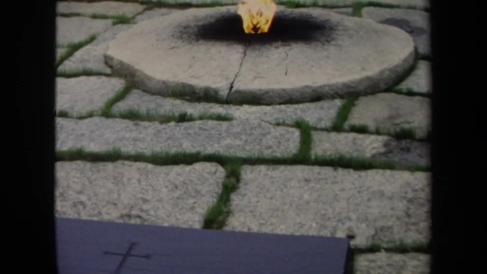 1970 Washington, DC 8mm frame showing the eternal flame on a circular stone base, with soot marks and cobblestone paving nearby.