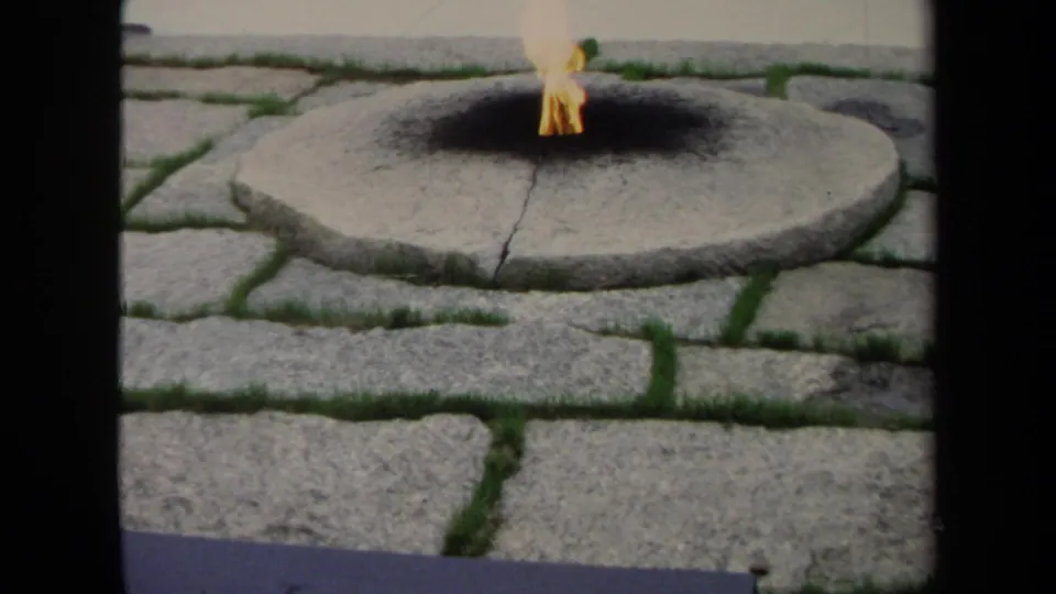 1970 Washington, DC frame holding on the eternal flame, circular stone base, blackened surface, and surrounding cobblestone paving.