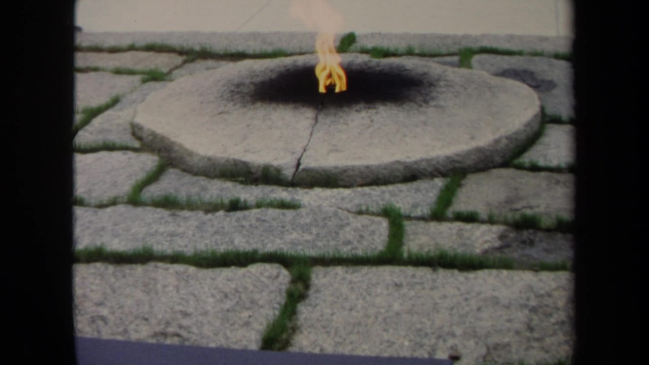 Small flame burning in a circular stone fire pit set among gray pavers.