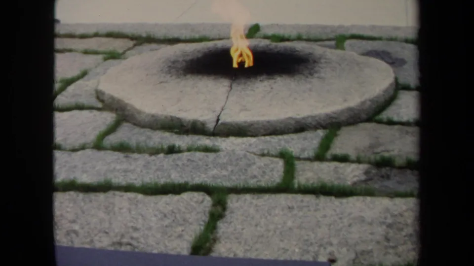 1970 8mm Washington, DC frame showing a small yellow flame in a circular stone fire pit with grass between surrounding pavers.