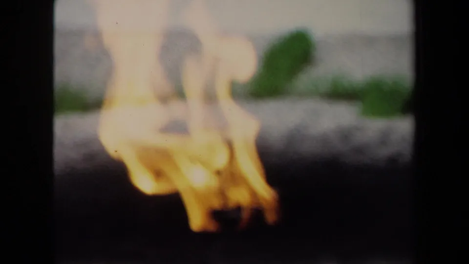 Soft 1970 8mm Washington, DC close-up of a bright flame in the foreground, with the stone fire pit and pavers blurred behind it.