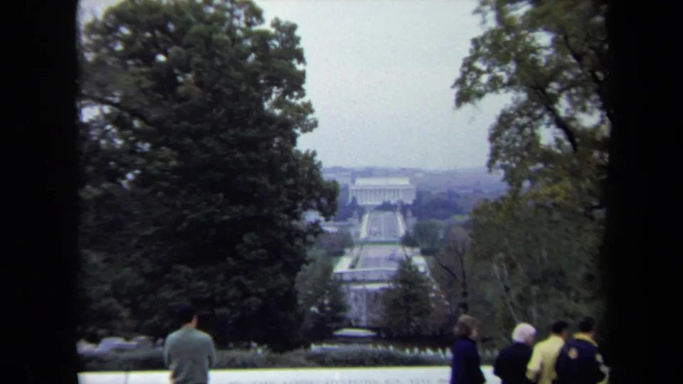 The final 8mm frame shows tourists at the lower edge of a tree-framed Washington, DC overlook, facing the Reflecting Pool and distant memorial structures.