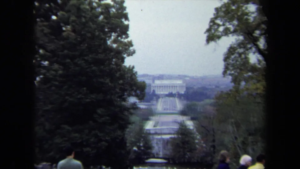 1970 Washington DC home-movie frame showing the Lincoln Memorial and Reflecting Pool through trees from a raised visitor viewpoint.