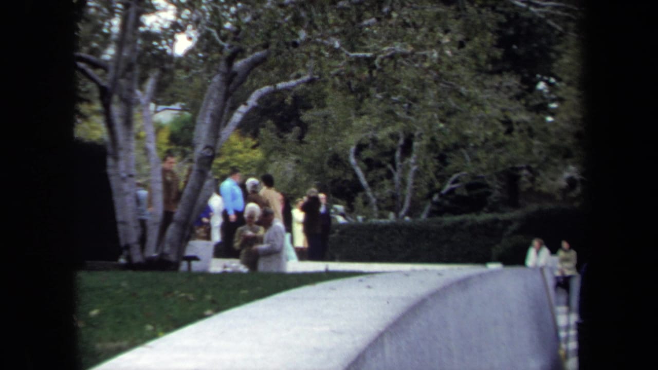 Home-movie view of a Washington, DC park path with small groups of visitors near trees and hedges in 1970.