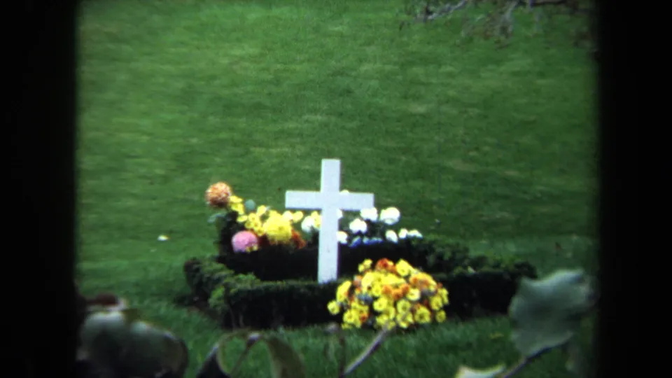 1970 Washington, DC 8mm frame showing the clearest view of the white cross grave marker and surrounding flowers on a lawn.