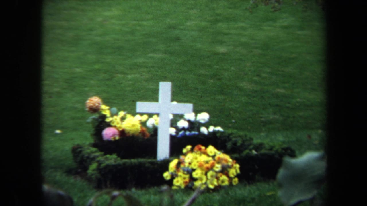White cross grave marker and flower arrangements seen from a similar close angle.