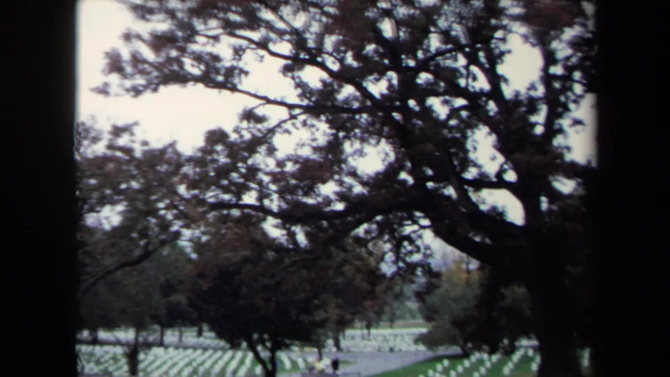 Wider 1970 8mm view of rows of white crosses across a grassy cemetery lawn under mature trees in Washington, DC.
