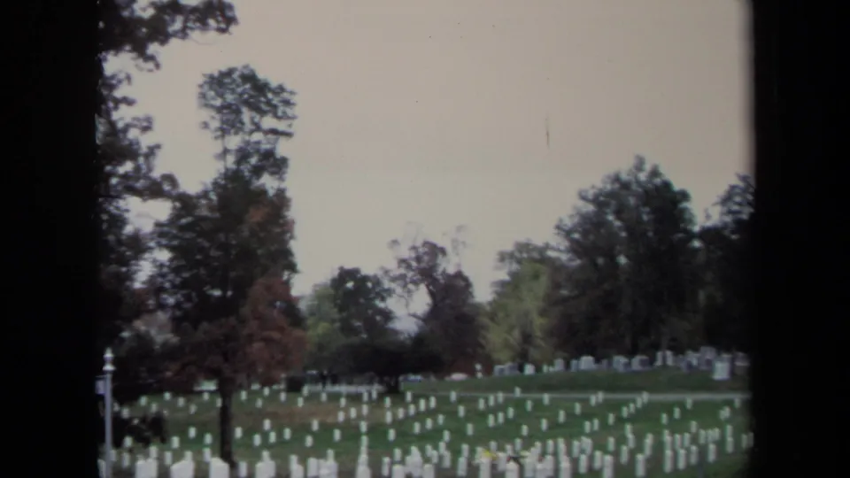 1970 8mm view across a Washington, DC cemetery, with white headstones receding through the lawn toward a tree line.
