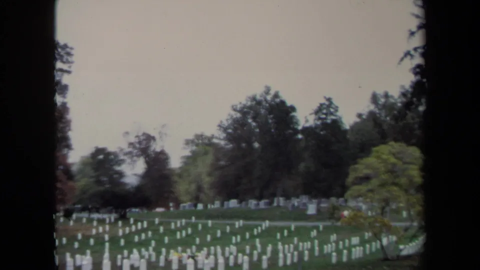 Soft 8mm frame of a Washington, DC cemetery in 1970, showing white grave markers across grass with trees beyond.