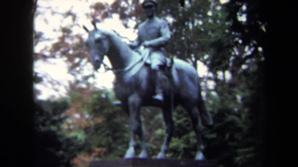 1970 Washington DC home-movie frame showing a bronze rider in a hat seated on a horse in a leafy park setting.