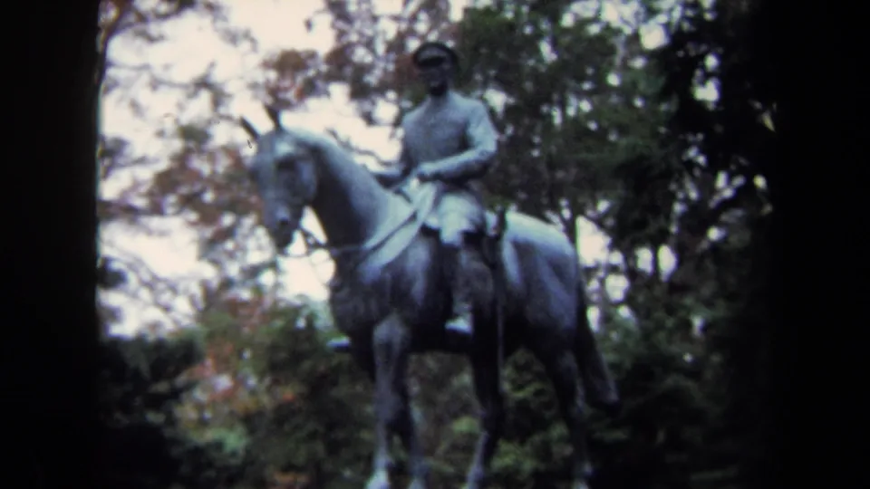 1970 Washington DC 8mm frame of an outdoor bronze equestrian statue, with the rider, horse, reins, and foliage visible.
