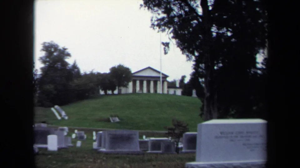 1970 Washington DC 8mm frame showing cemetery grounds below a classical colonnaded building and flagpole.