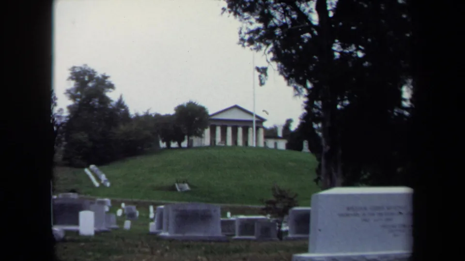 Final 1970 Washington DC 8mm view across grave markers toward a hilltop classical building under trees.