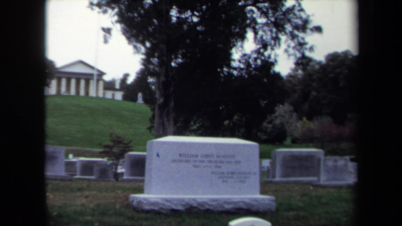 McAdoo gravestone in a cemetery with headstones, trees, and a classical building in the background.