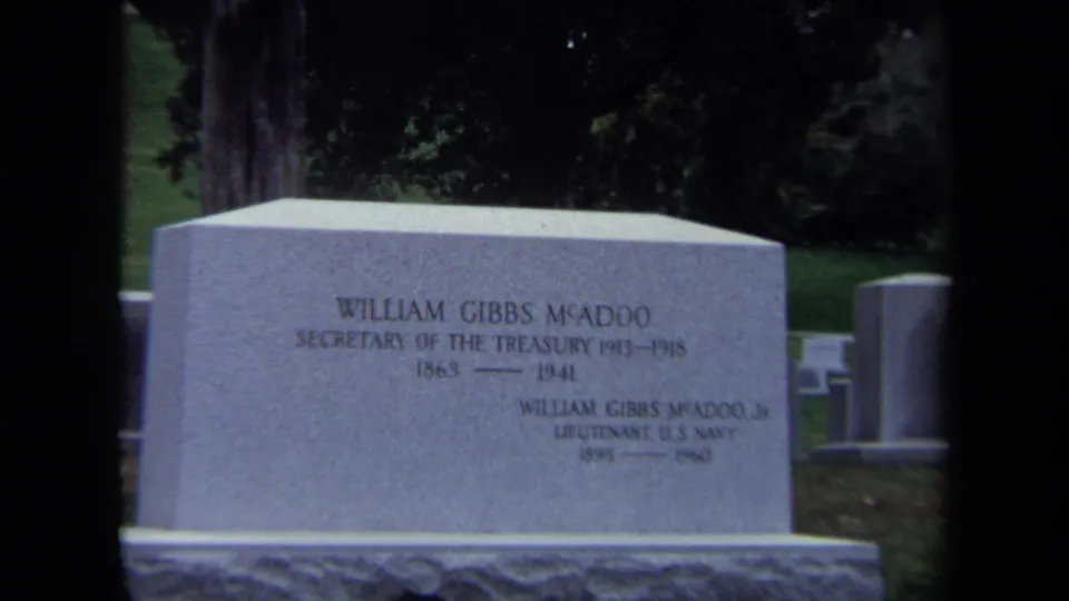Close 1970 8mm frame of the William Gibbs McAdoo gravestone inscription, including Treasury and family text, in a cemetery setting.